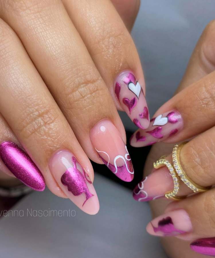 A imagem retrata um par de mãos com unhas pintadas de rosa - tendência Barbiecore. Os esmaltes usados são de cor: rosa glitter, branco, nude, preto. O esmalte está uniforme e brilhante. As unhas estão no formato oval.