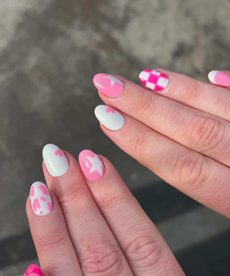 A imagem retrata um par de mãos com unhas pintadas de rosa. Os esmaltes usados são de cor: pink e branco. O esmalte está uniforme e brilhante. As unhas estão no formato redondo.