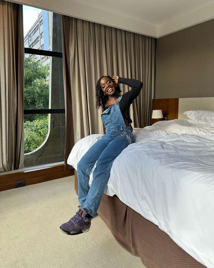 Foto da atriz sentada em cama de quarto de hotel luxuoso
