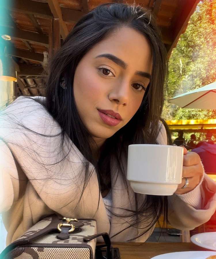 Selfie da influenciadora Mariely Santos, em café, sentada em mesa e segurando xícara - procedimentos estéticos favoritos das famosas