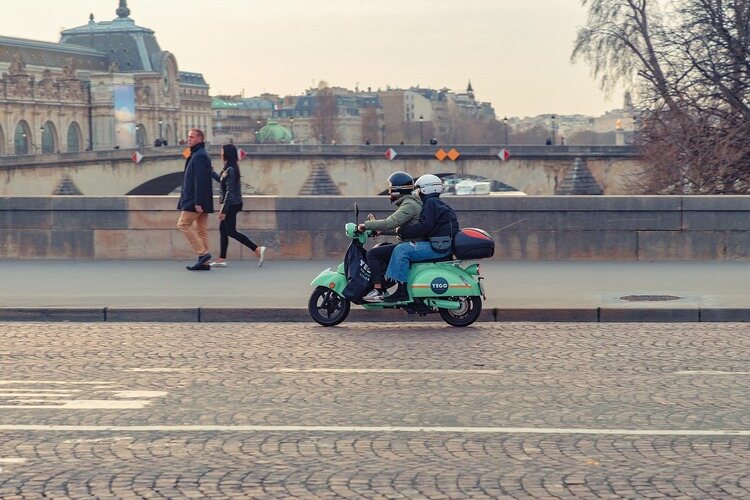 duas pessoas em cima de uma scooter azul passeando por Paris