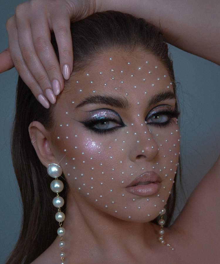 Mulher maquiada com trends de make 2023: pedraria, foxy eys, glitter, iluminação, boca contornada