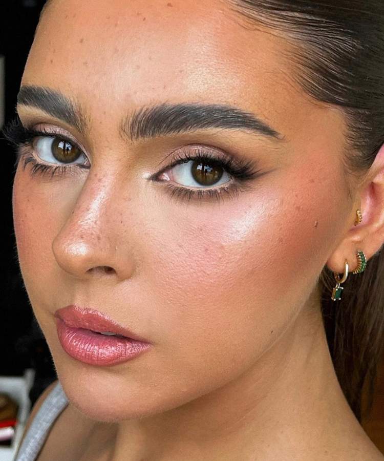 Mulher maquiada com trends de make 2023: pele glow com iluminação, foxy eyes, sardas