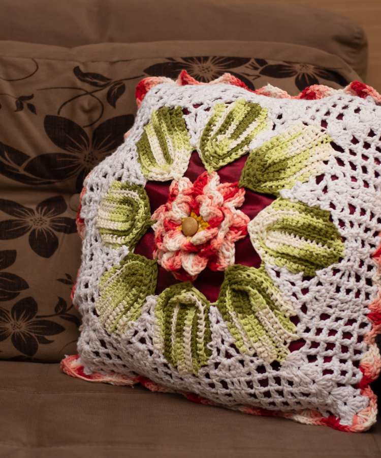 Sofá com almodafa e capa de crochê, cortes branco, verde, vermelho, rosa no meio e folhas