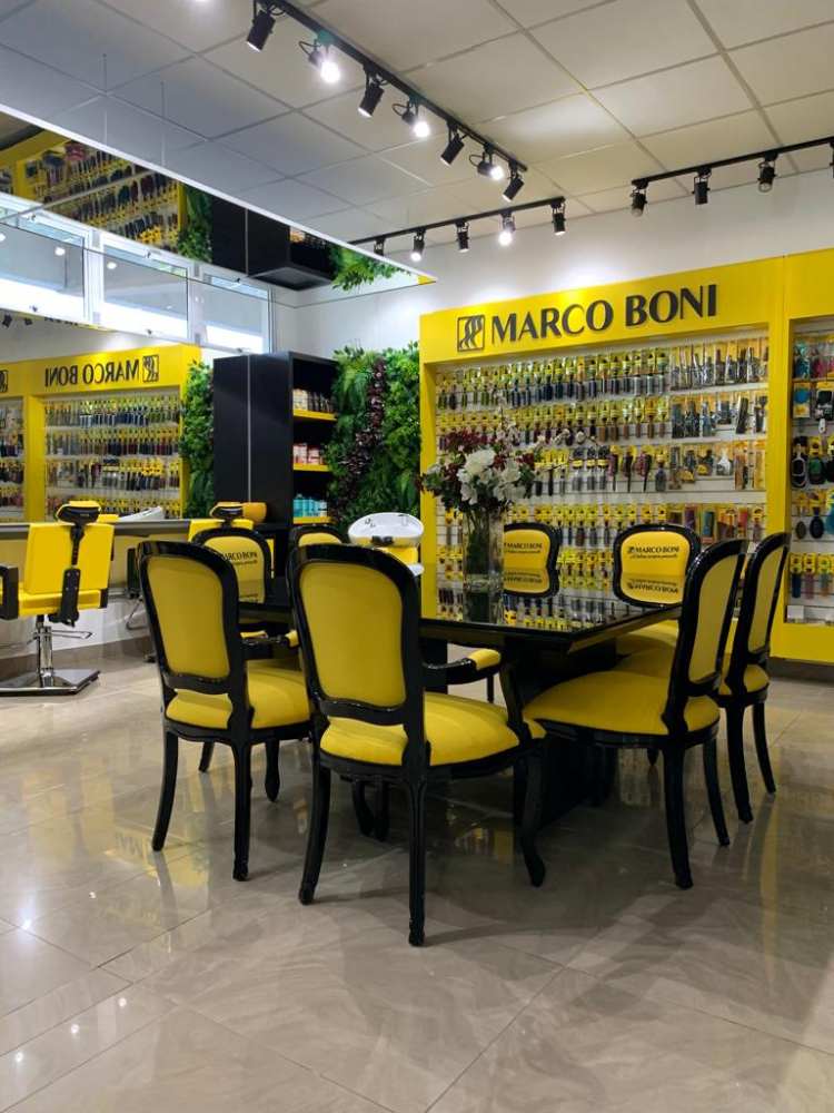Empresa Marco Boni por dentro, mesa preta com cadeiras amarelas, exposição de produtos