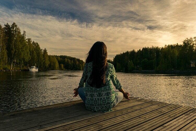 mulher meditando em frente a um lago