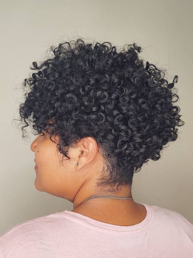 Mulher de pele negra de perfil usando cabelo cacheado curto em pixie repicado