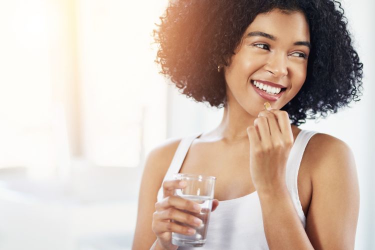 Mulher de pele negra sorridente, tomando suplemento e segurando copo com água