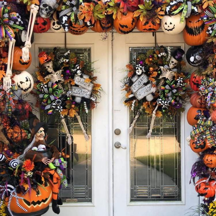 Entrada de casa com porta branca dupla decorada com flores, abóboras, esqueletos, teias e mais 