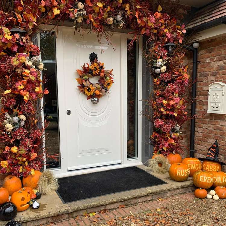 Entrada de casa com porta branca cercada de flores laranjas e abóboras