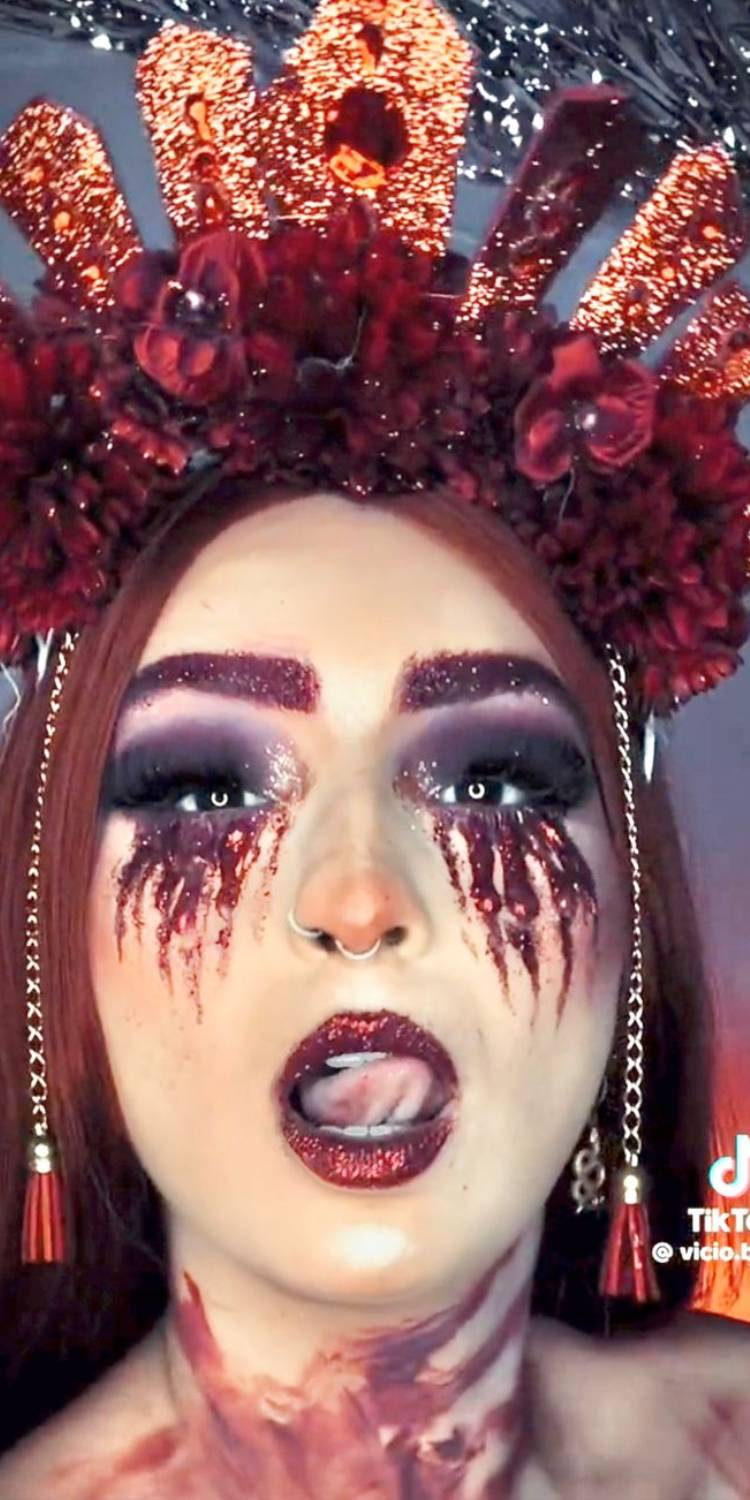 Mulher ruiva com maquiagem de lágrumas vermelhas, sombra escura e tiara de Halloween vermelha com corrente e flores