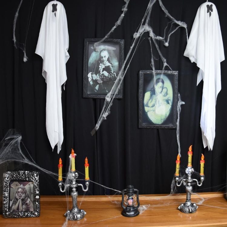 Decoração de Halloween com fundo preto, fantasmas feitos de panos brancos pendurados, imagens antigas e velas em castiçais