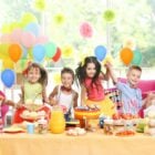 Foto de crianças sorrindo atrás de mesa com doces, decorada em amarelo e com bexigas coloridas