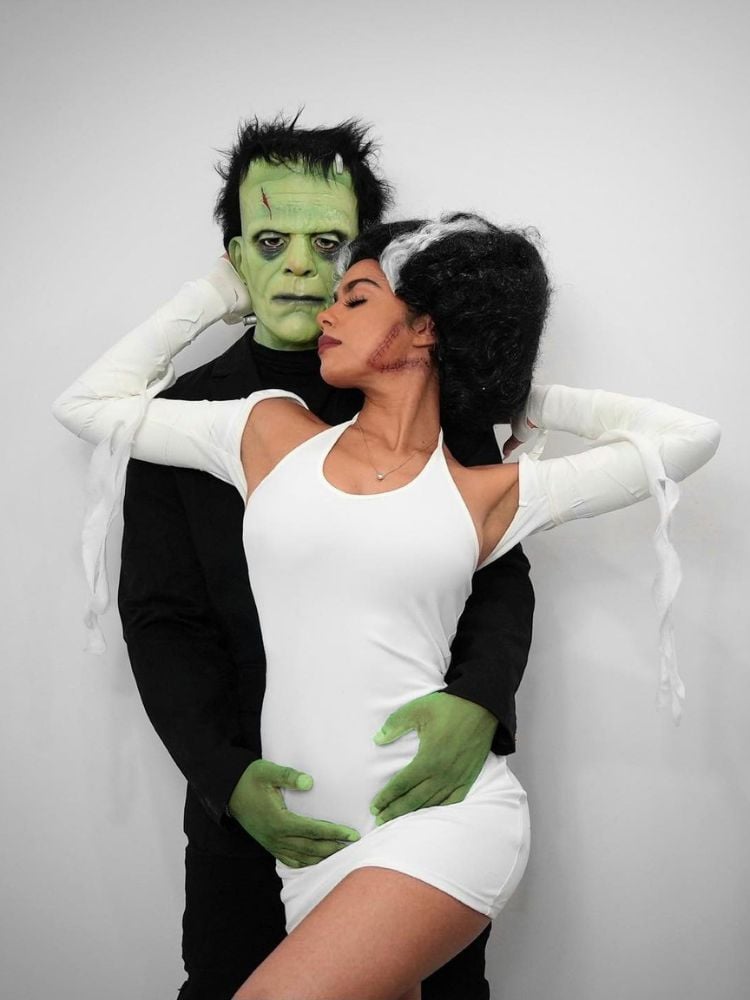 Homem de roupa preta e máscara de Frankenstein e mulher de vestido branco e cabelo preto e branco colmeia 