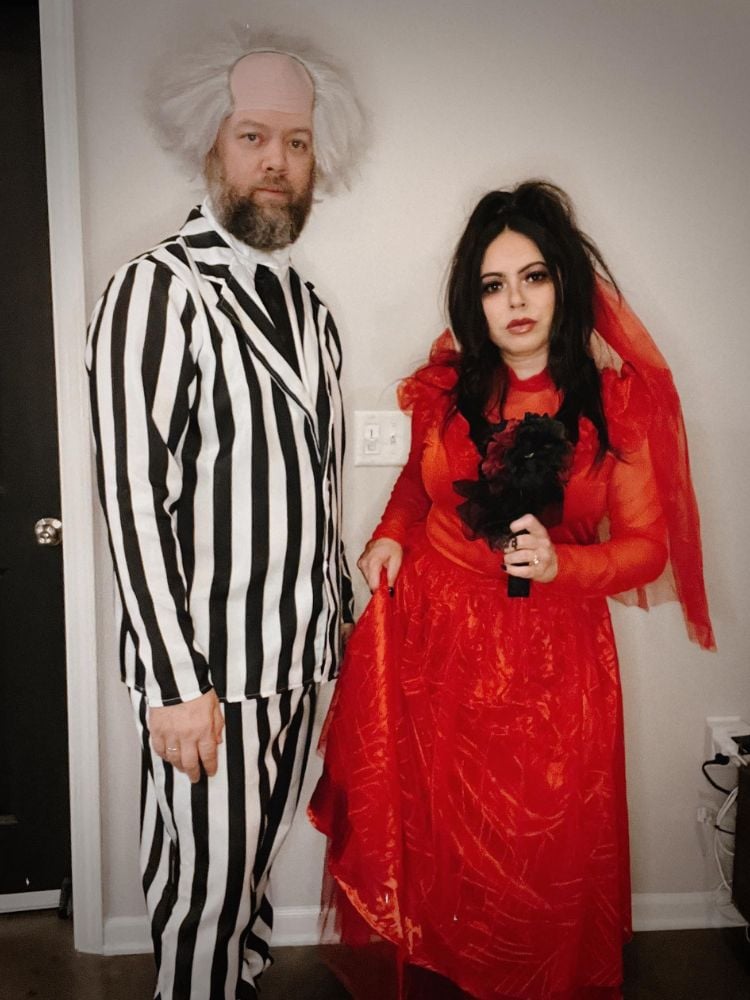 Homem com terno listrado preto e branco e peruca de cabelo branco desajeitado e mulher usando vestido vermelho e véu vernelho 