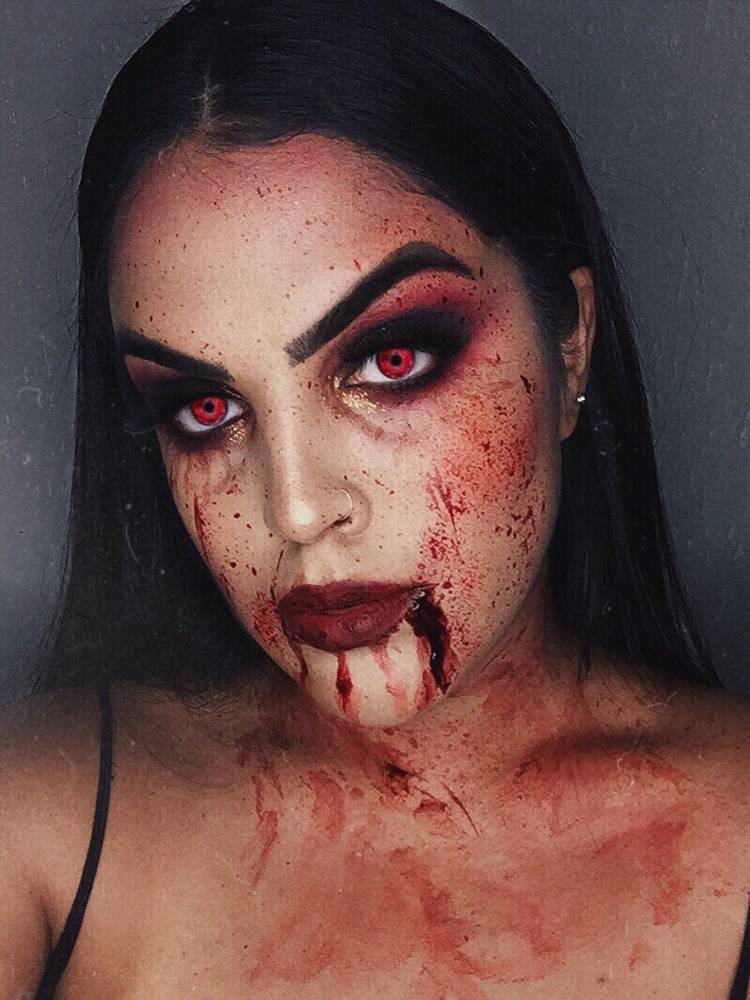 Mulher de pele clara usando maquiagem vermelha e preta nos olhos, batom vermelho e sangue por todo o rosto 