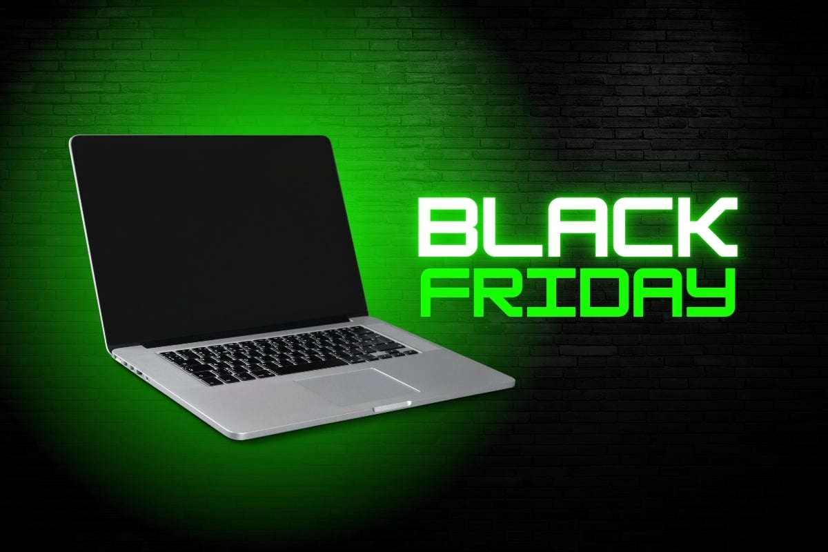 A imagem mostra um laptop aberto sobre um fundo de tijolos iluminado por uma luz verde. Ao lado do laptop, a frase "Black Friday" está em destaque com letras grandes e brilhantes, também em verde. A cena sugere um anúncio promocional, enfatizando ofertas especiais de tecnologia para a Black Friday.