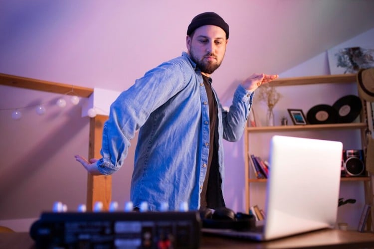 Homem de pele clara usando blusa preta e camisa azul fazendo mímica em frente ao notebook