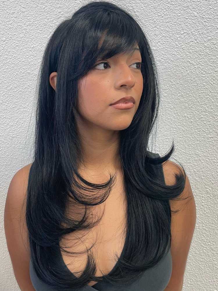 Mulher de pele morena e rosto redondo usando regata preta e cabelo longo com franja lateral preta