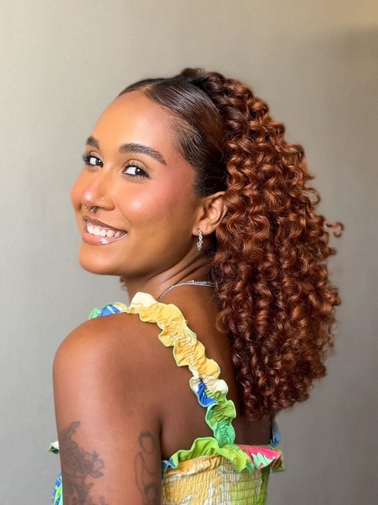 Mulher de pele negra com gel na franja e cabelo solto cacheado