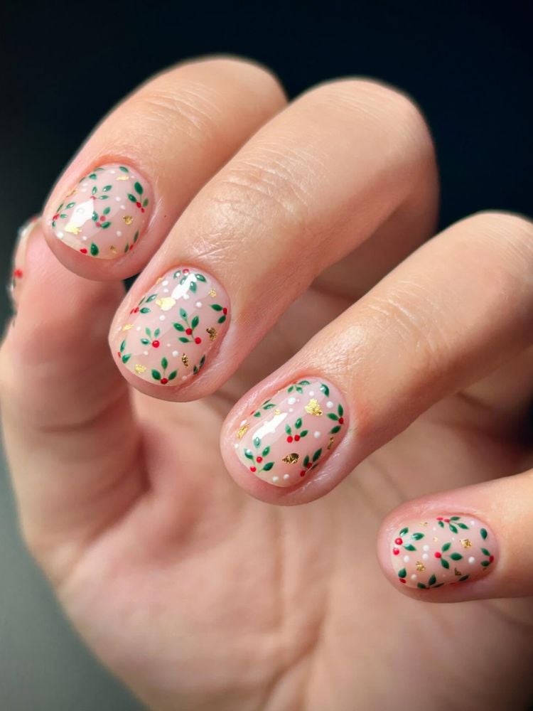 Mão de pele clara com unhas bem curtinhas, de fundo transparente e com desenho de frutas vermelhas de natal