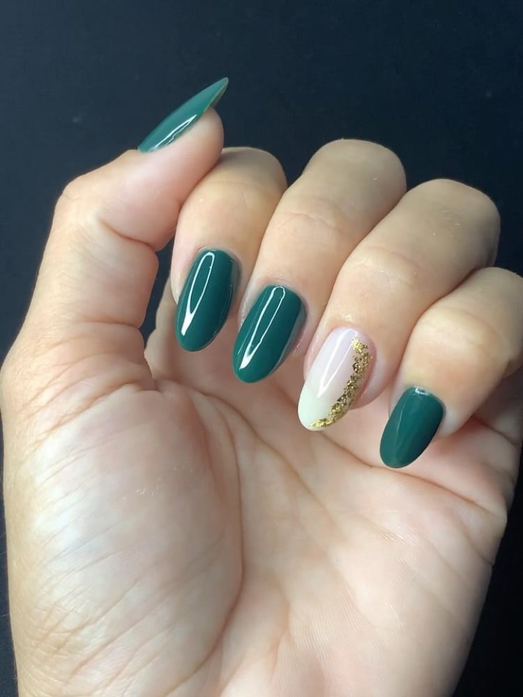 Mão de pessoa de pele clara com unhas almond em verde e anelar em nude com folah de ouro 