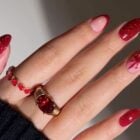 Mão de pele clara com unhas almond em vermelho com glitter e nudes com francesinha e laço