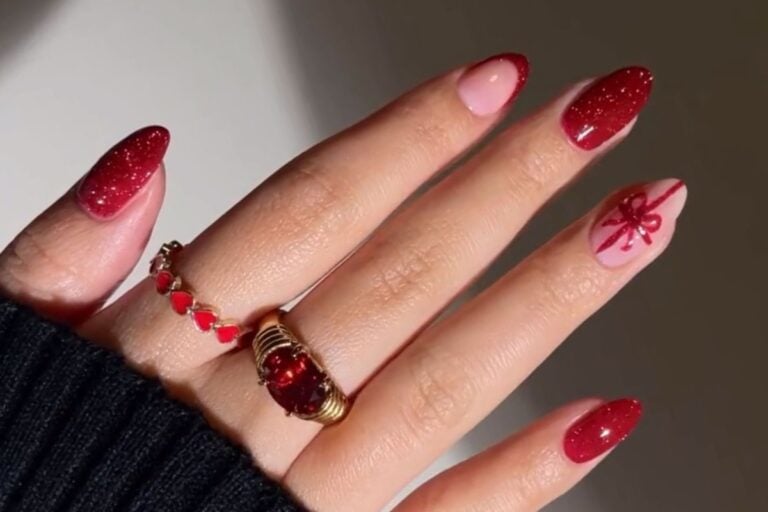 Mão de pele clara com unhas almond em vermelho com glitter e nudes com francesinha e laço