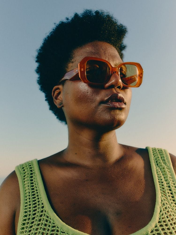 foto de mulher negra usando óculos de sol do modelo Elza, da collab entre as marcas Zerezes e Haight, e regata de crochê verde