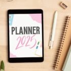 Mesa bege com cadernos, planta, óculos, caneta e tablet com planner 2025 em rosa, azul e preto