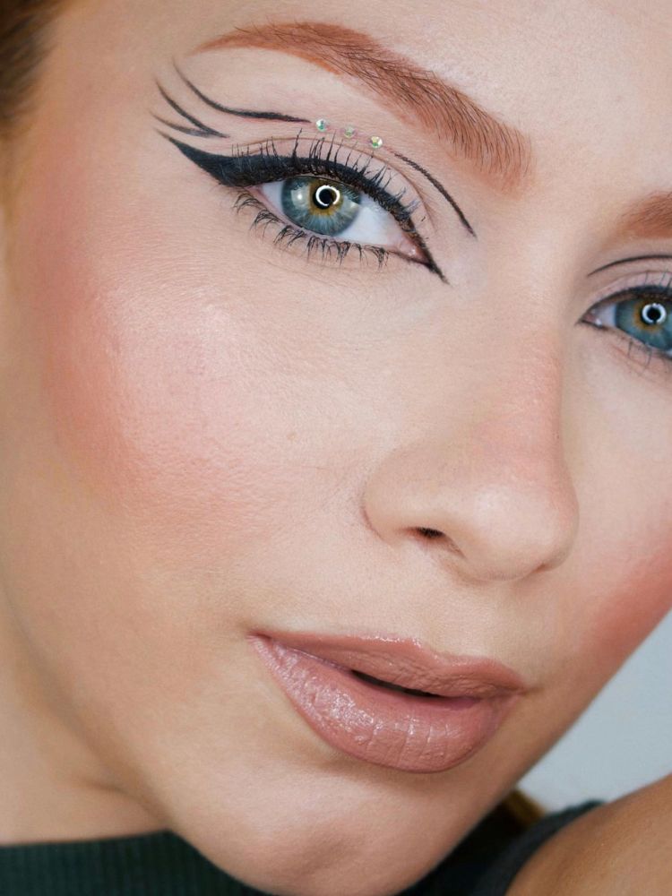 Mulher de pele clara e olhos azuis usando delineado gráfico, strass e gloss