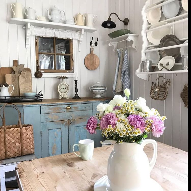 Jarro com flor sob uma mesa de madeira em uma cozinha com prateleiras e utensílios de cerâmica
