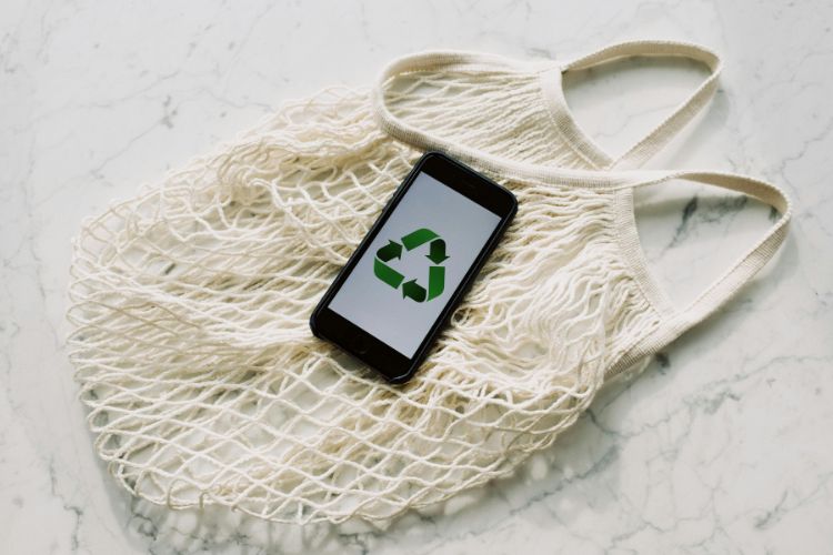Pedra de mármore com sacola ecológica e celular com símbolo de reciclagem na tela, simbolizando a sustentabilidade das empresas espiritualizadas
