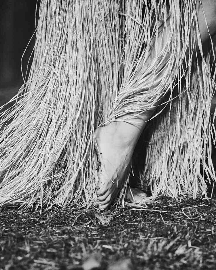Foto de Anitta com os pés descalçoes e palha que representa Omolu e Obaluaê no Candomblé