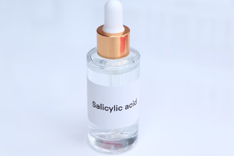 Foto de fundo azul com sérum transparente em embalagem conta-gotas com rótulo escrito "salicylic acid"