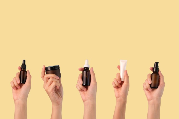 Foto de fundo laranja com várias mãos de pele clara segurando produtos de skincare