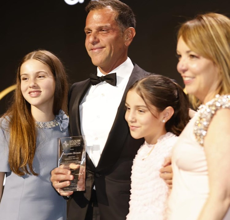 Alexandre Birman ganha premiação "Melhor Pessoa do Ano 2024", está de terno ao lado de suas filhas e de sua mãe.