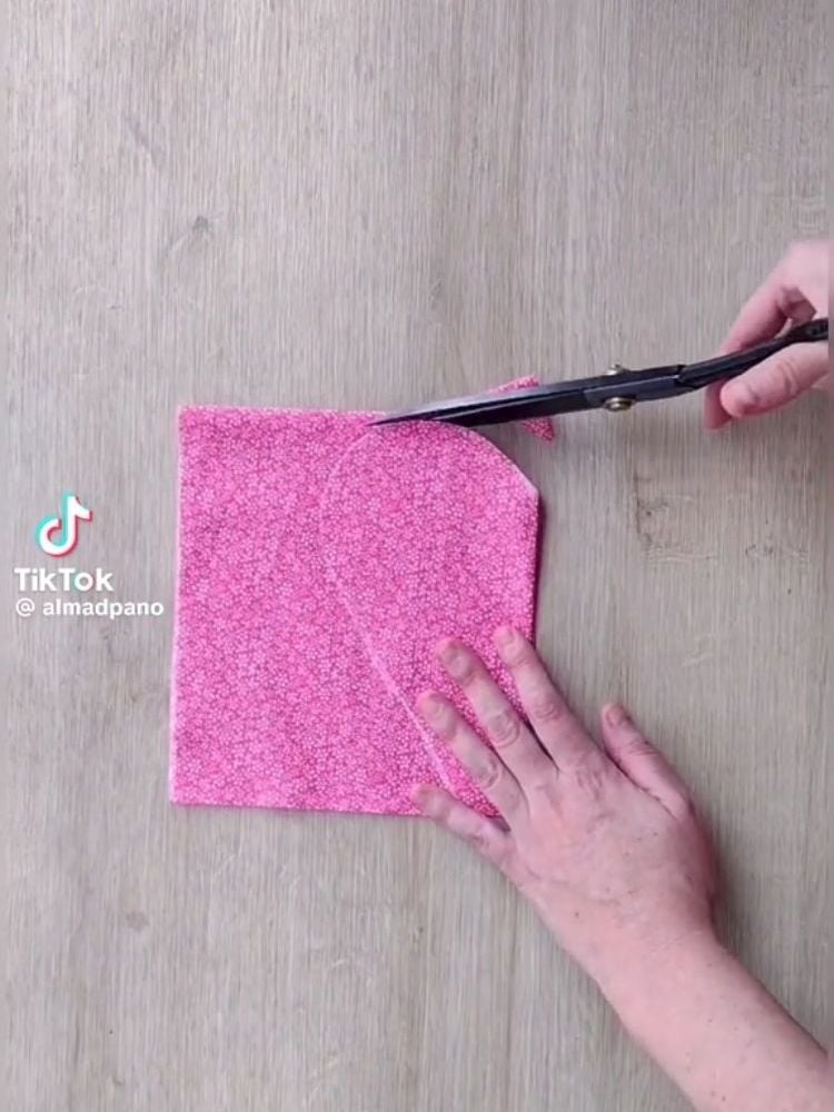 Pessoa de pele clara cortando tecido rosa em formato de coração
