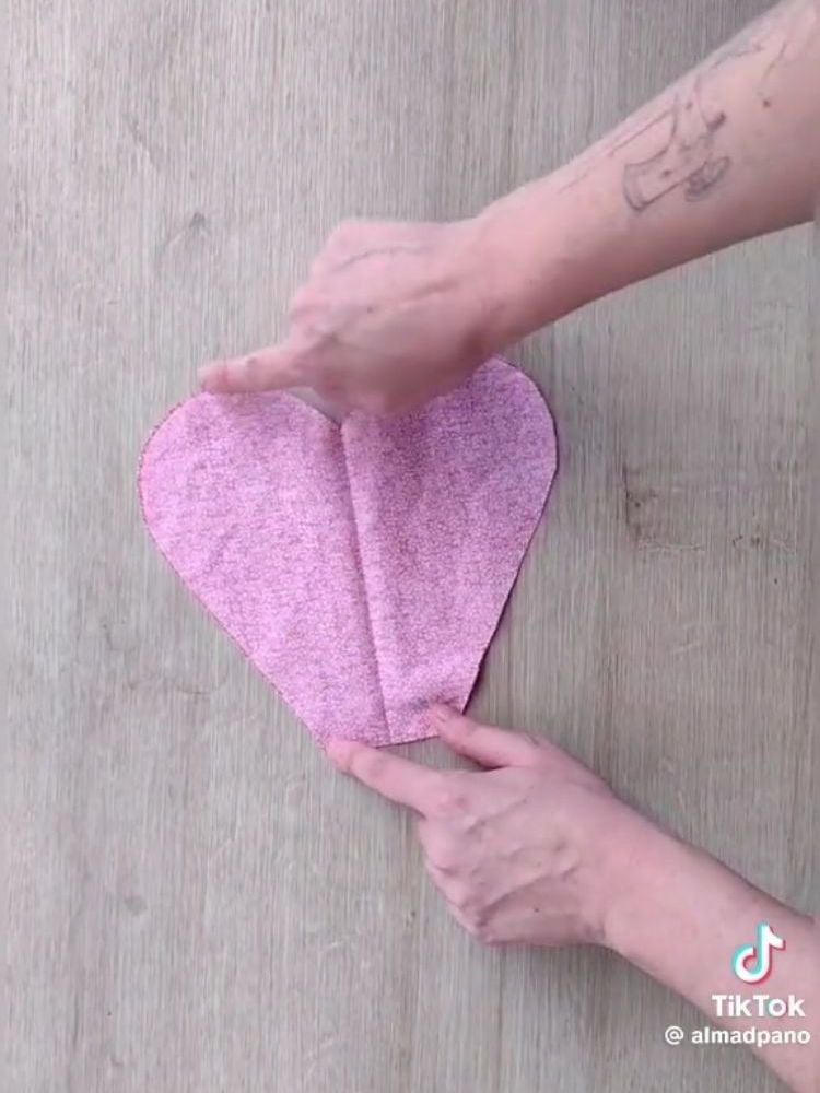 Pessoa de pele clara apontando o dedo sobre tecido rosa em formato de coração