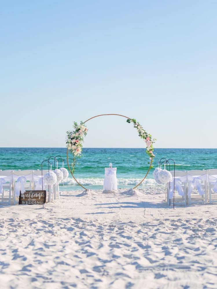 Casamento na praia com arco simples, de poucas flores e cadeiras brancas