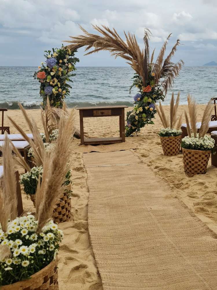 Passarela de casamento na praia com galhos secos, arco com galhos secos e flores coloridas