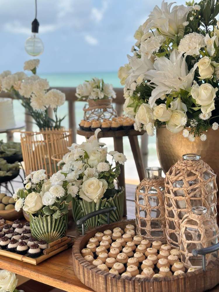Mesa de doces de casamento na praia, com flores brancas e diferentes docinhos