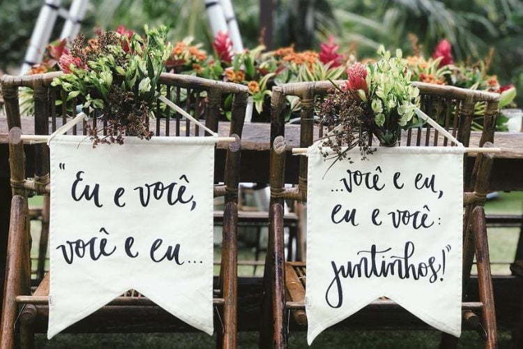 Cadeiras de madeira em casamento com flores e flâmula branca com frases