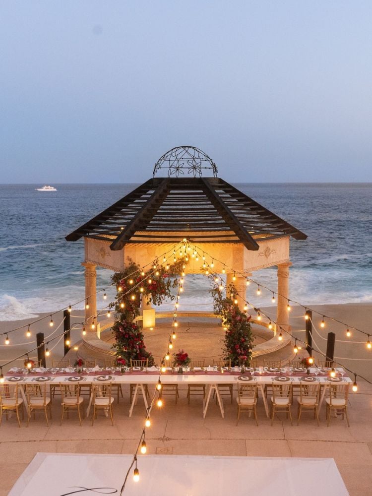 Decoração de casamento na praia com estrutura, arco de flores, cadeiras e várias luzes de corda