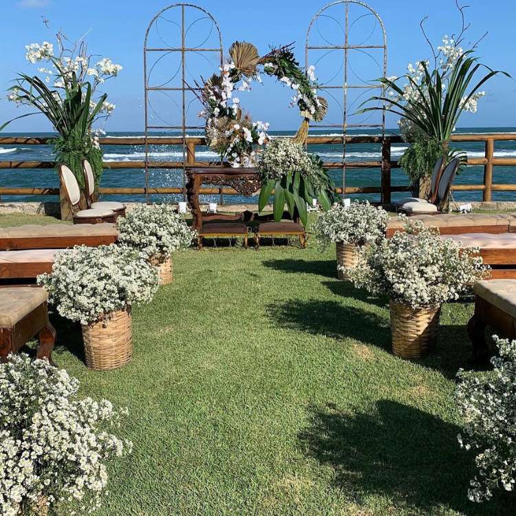 Casamento na praia com muitas flores e bancos para os convidados 