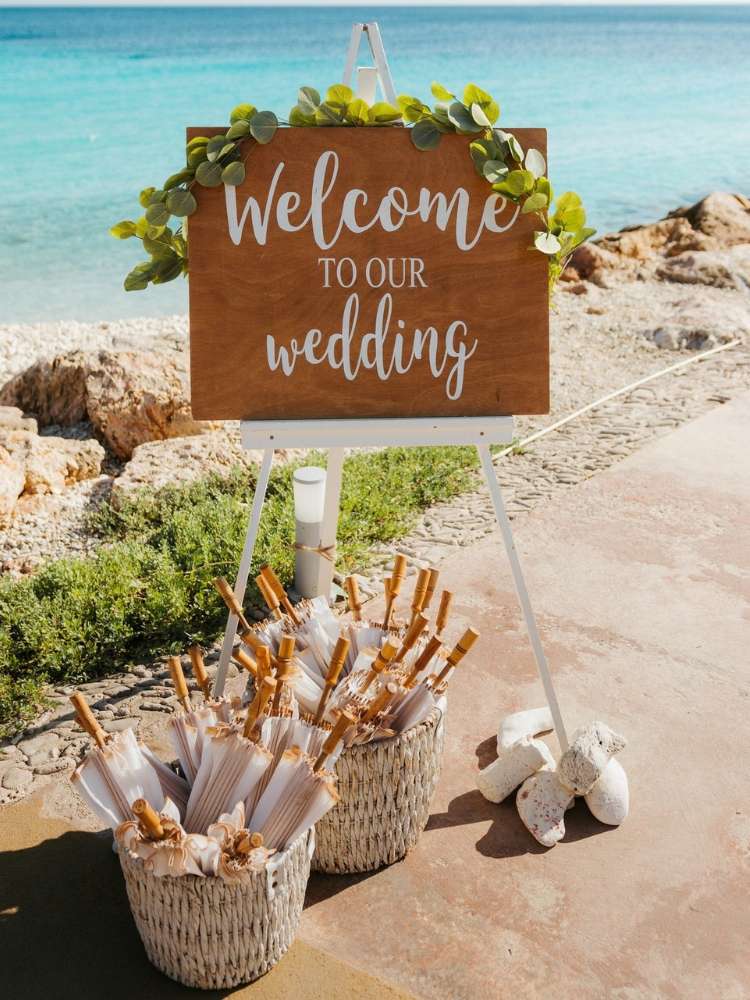 Casamento na praia com placa de madeira de boas vindas dizendo "Welcome to our wedding"