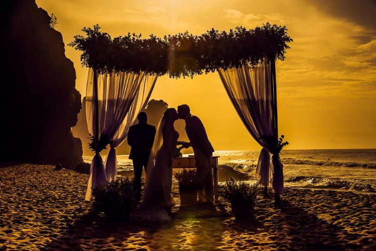 Foto de noivos se beijando em casamento na praia durante o pôr do sol