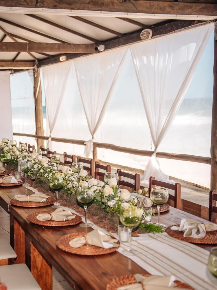 Mesa posta em casamento na praia com flores brancas, guardanapo de tecido bege e sousplat de palha