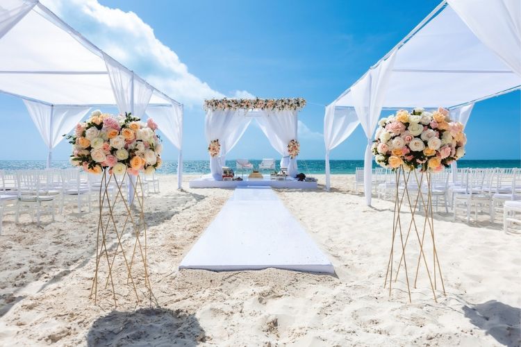 Cenário de casamento na praia com tendas de tecido e arranjos florais
