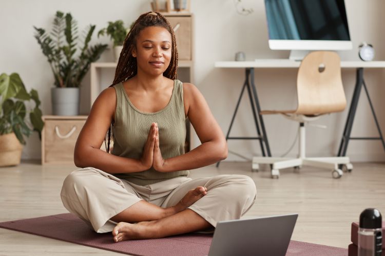 Mulher meditando em casa em frente a um notbook